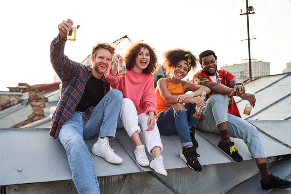 Šťastní čtyři lidé slaví na střeše města — Stock fotografie