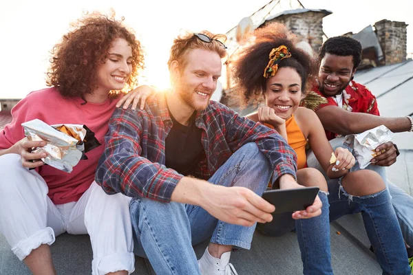 Glada vänner med smartphone äta snacks på taket — Stockfoto