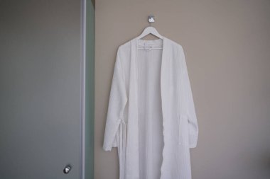 Banyodaki kahverengi duvarda beyaz bornoz var.