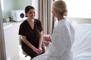 Genç kozmetik uzmanı güzellik kliniğindeki kadın müşteriye bakıyor.