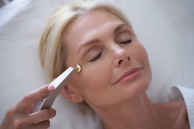 Güzellik uzmanı, göz kenarlarındaki kırışıklıkları düzeltmek için bir cihaz kullanıyor.