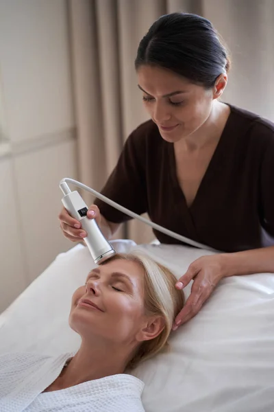 Leende kosmetolog håller en modern anordning för ansiktsbehandlingar — Stockfoto