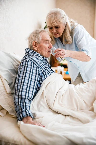 Mujer ayudando a beber una píldora a su marido — Foto de Stock