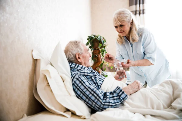 Wife giving pills and water to her husband — Stock Photo, Image