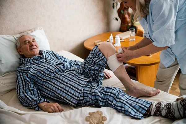 Mujer aplicando vendaje a su marido pierna —  Fotos de Stock