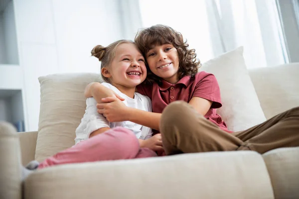 Chica con hermano es abrazando en sofá — Foto de Stock