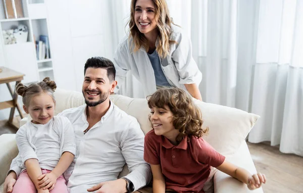 Kinderen zitten op de bank met vrolijke ouders — Stockfoto