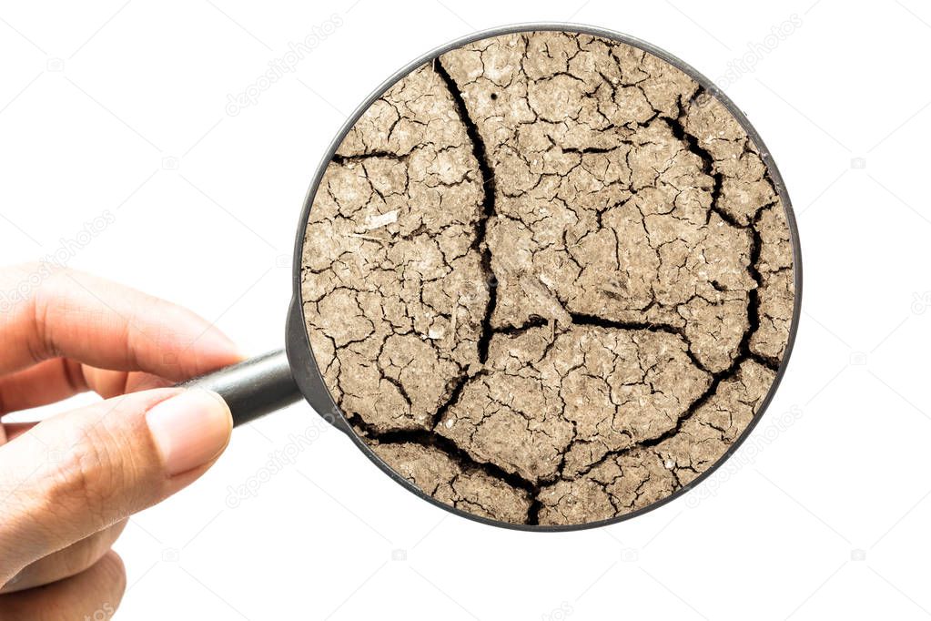 Hand holding magnifying glass with cracked dry earth isolated on white background