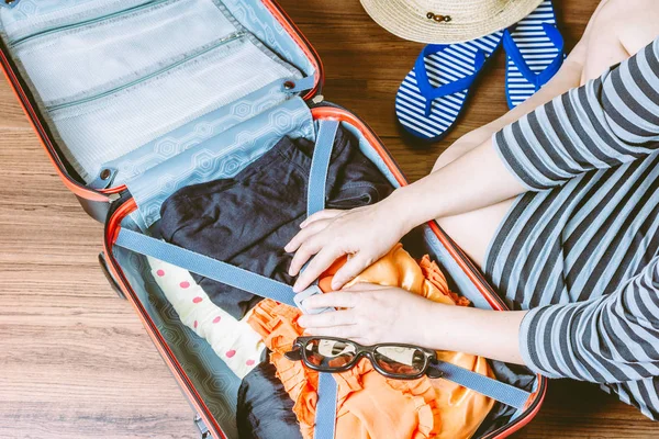 Woman packing a luggage on wooden floor