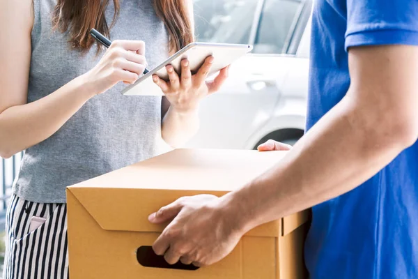 Woman putting signature in tablet on cardboard box with delivery man