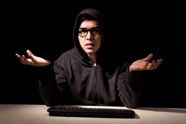 Hacker in a hood stealing information with computer on dark background clipart