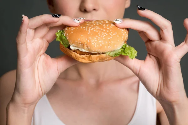 Young woman eating hamburger on gray background. Junk food and fast food concept