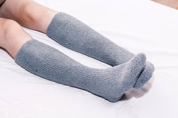 Woman legs in knee socks on white bed at home