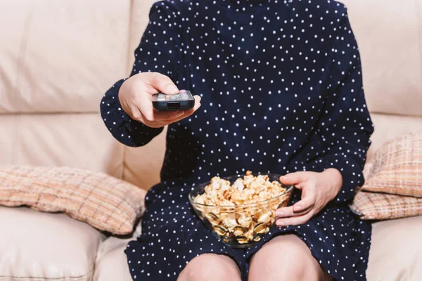 Woman holding remote control and eating popcorn on sofa