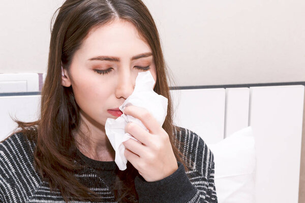 Sick woman blowing her nose with tissues