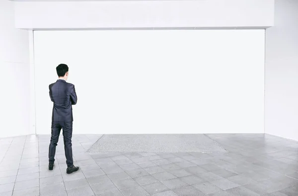 Businessman in black suit standing in empty interior with mock up white space