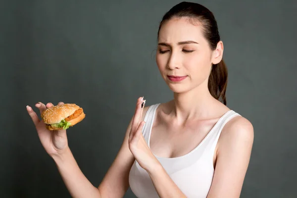 Young woman eating hamburger on gray background. Junk food and fast food concept