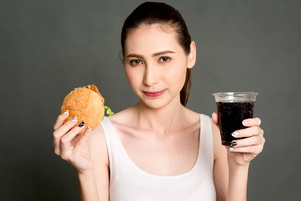 在灰色背景下吃汉堡包和可乐的年轻妇女 垃圾食品与快餐概念 — 图库照片