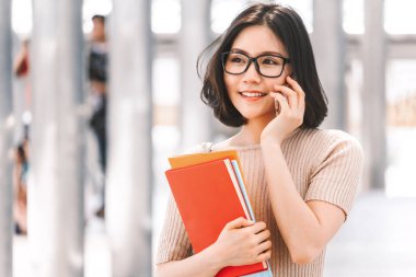 Kitap yürüyüş ve kampüs içinde bir smartphone kullanarak tutan genç üniversiteli kadın