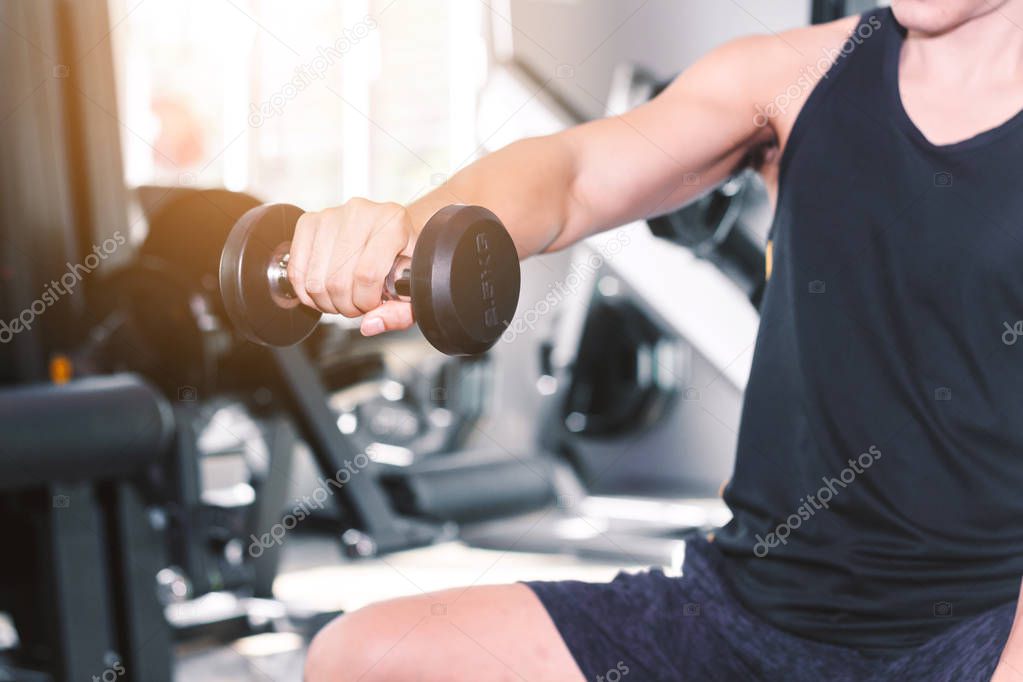 Fitness man doing weights exercises with dumbbell sitting at the gym