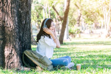 Kadın sakin Park çimenlerin üzerinde oturan müzik dinlerken kulaklık ile