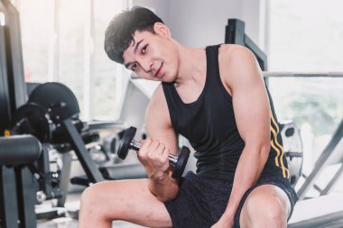 Spor salonunda oturan dumbbell ile ağırlık egzersizleri yapıyor fitness adam