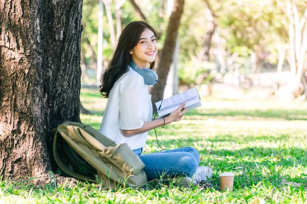 学生の若い女性がリラックスして 公園の草の上に座って本を読んで — ストック写真