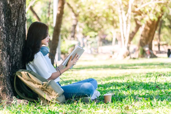 学生の若い女性がリラックスして 公園の草の上に座って本を読んで — ストック写真