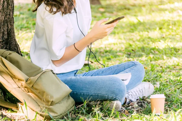 女性がリラックスして 公園の芝生の上に座っているスマート フォンを使用 — ストック写真