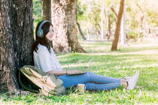 Kadın dinlenmek ve Park çimenlerin üzerinde oturan bir dizüstü bilgisayar kullanarak