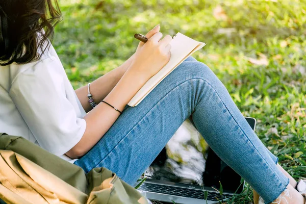 公園の芝生の上に座ってノートを書くペンを持つ女性 — ストック写真