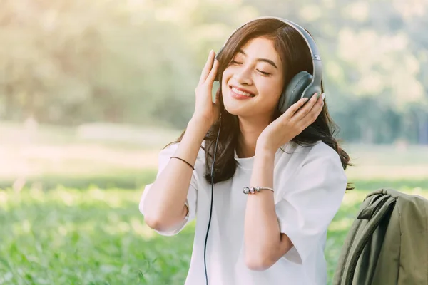 女性は 公園の草の上に座って音楽を聴くヘッドフォンでリラックスします — ストック写真