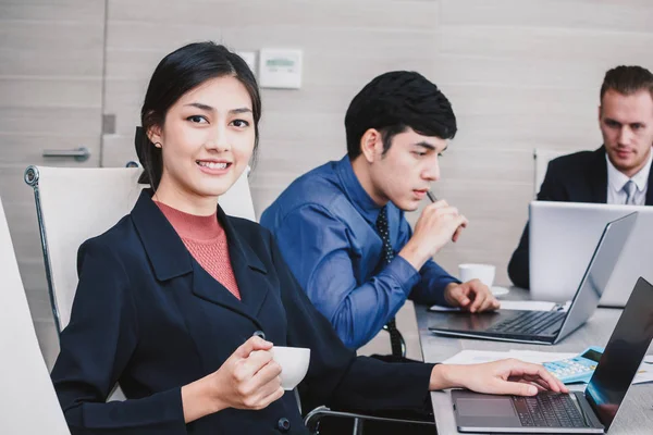 Gülümseyen ve bir iş toplantısı sırasında kameraya bakarak işkadını