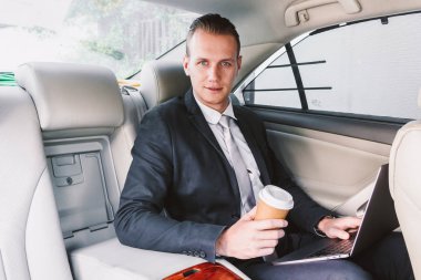 Bir arabanın arka koltuğunda oturan dizüstü bilgisayar üzerinde çalışan yakışıklı işadamı