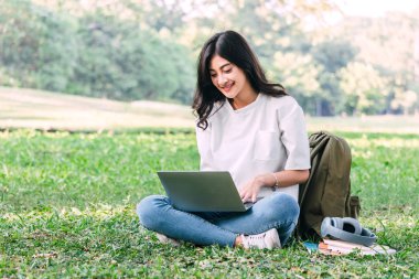 Kadın dinlenmek ve Park çimenlerin üzerinde oturan bir dizüstü bilgisayar kullanarak