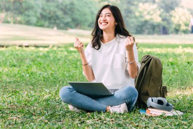 Kadın dinlenmek ve Park çimenlerin üzerinde oturan bir dizüstü bilgisayar kullanarak