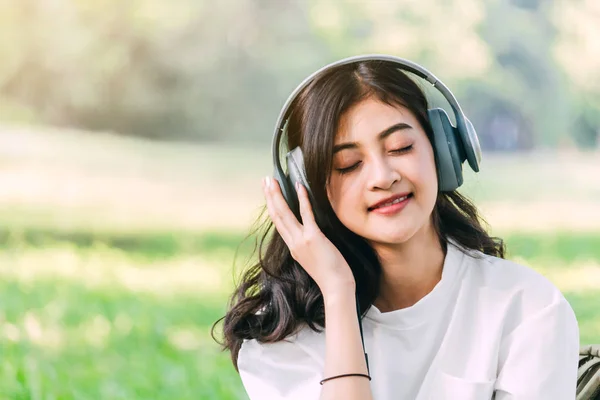 女性は 公園の草の上に座って音楽を聴くヘッドフォンでリラックスします — ストック写真