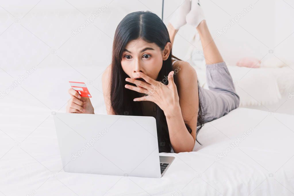 Woman shopping online with notebook on bed at home