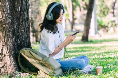 Kadın sakin Park çimenlerin üzerinde oturan müzik dinlerken kulaklık ile