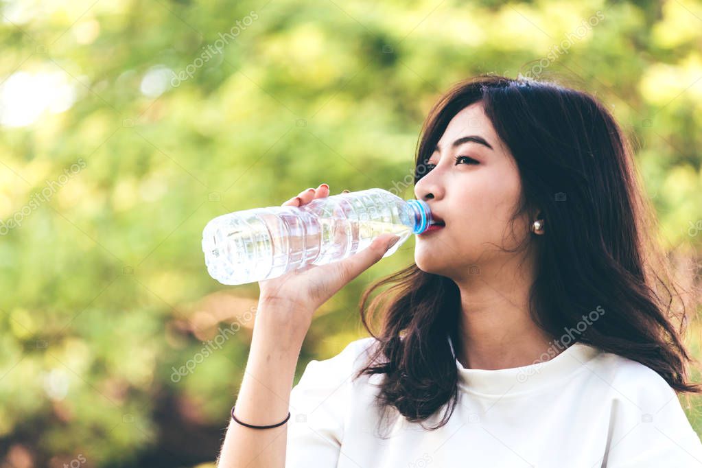 Beautiful woman drinking water at summer green park. Healthy lifestyle concept