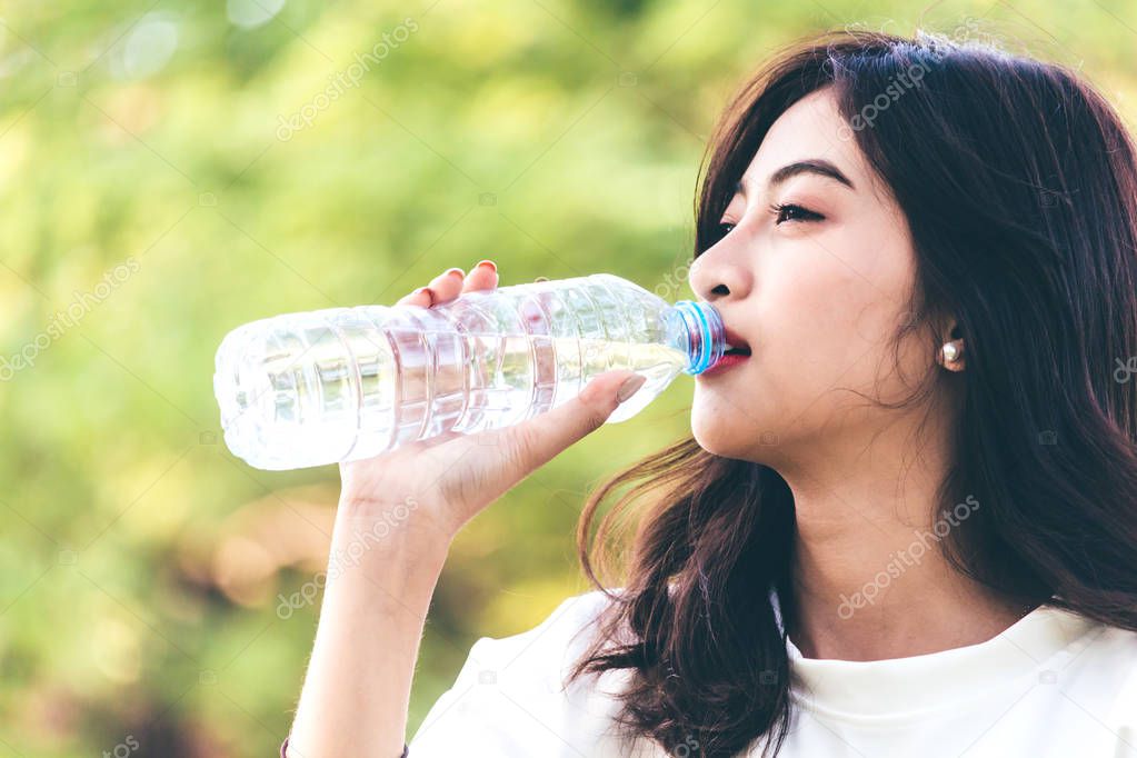 Beautiful woman drinking water at summer green park. Healthy lifestyle concept