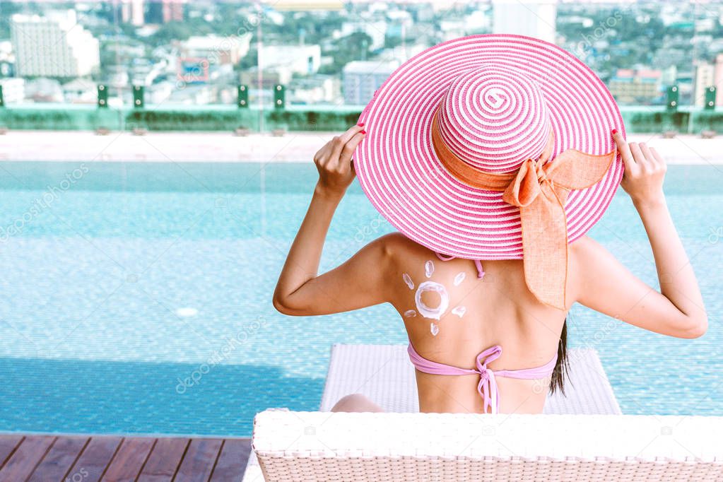 Woman applying suncream with sun drawn on back at resort spa pool