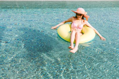 İki giyen kadın kauçuk halka yüzme havuzunda koltuklarda bikini yaz tatile rahatlatıcı resort spa adlı parça