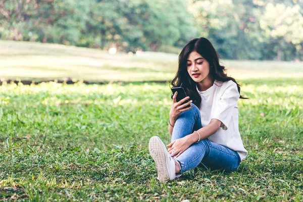 女性がリラックスして 公園の芝生の上に座っているスマート フォンを使用 — ストック写真