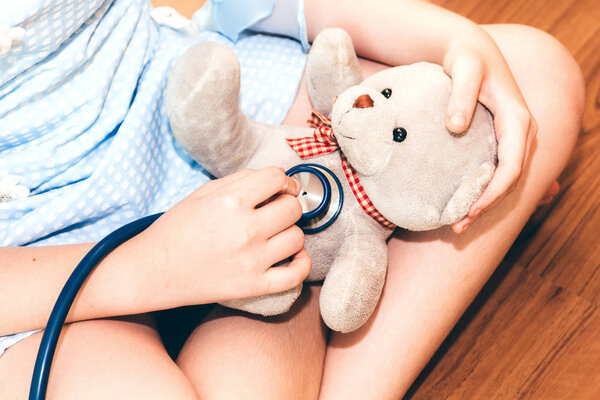 little girl playing doctor using stethoscope listening to teddy bear breath