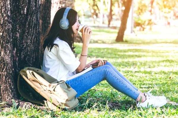 女性は 公園の草の上に座って音楽を聴くヘッドフォンでリラックスします — ストック写真