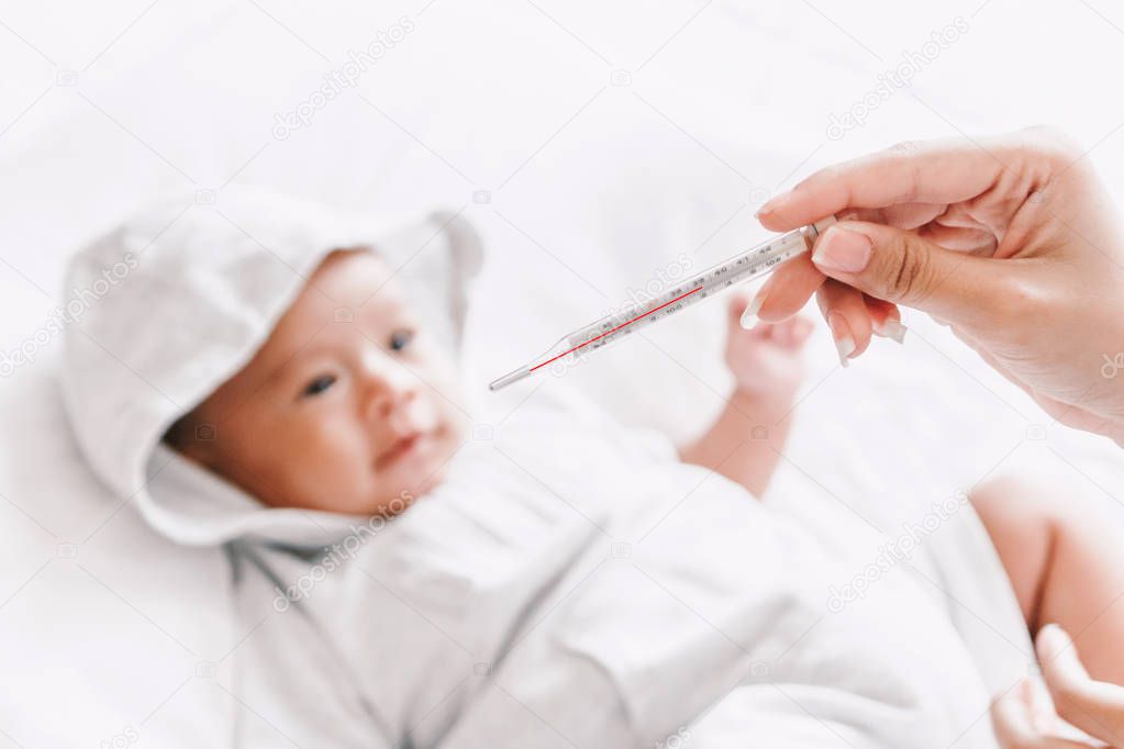 Mother holding thermometer of her ill baby.Sick baby on bed with fever measuring temperature 