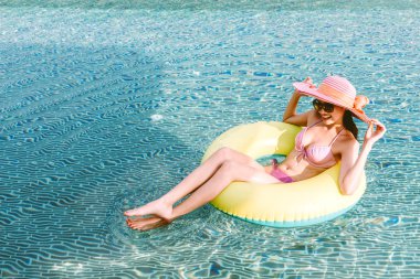 İki giyen kadın kauçuk halka yüzme havuzunda koltuklarda bikini yaz tatile rahatlatıcı resort spa adlı parça