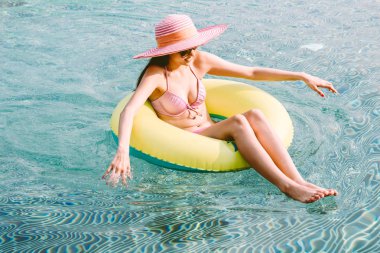 İki giyen kadın kauçuk halka yüzme havuzunda koltuklarda bikini yaz tatile rahatlatıcı resort spa adlı parça