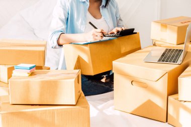 Genç kadın bağımsız çalışma ve denetim listesi ve karton siparişle yazma yatağa evde - KOBİ iş online ve teslimat kavramı kutu